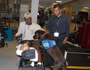 Deuce, a therapy dog at Walter Reed, and his owner Harvey Naranjo greet Sgt. 1st Class Andrew R. Allman, one of the patients at the occupational therapy gym.