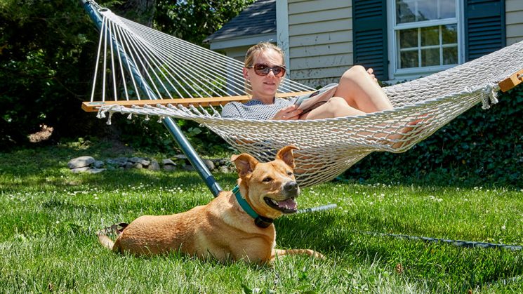 Dog sitting in the grass next to woman in hammock reading